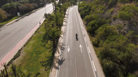 Rising-drone-shot-behind-a-couple-riding-a-motorbike-in-Marbella-Spain