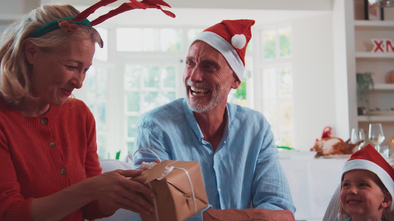 다세대 가족들이 산타 모자와  ⁇ 을 입고 집에서 크리스마스를 축하하고 선물을 열고 있습니다.
