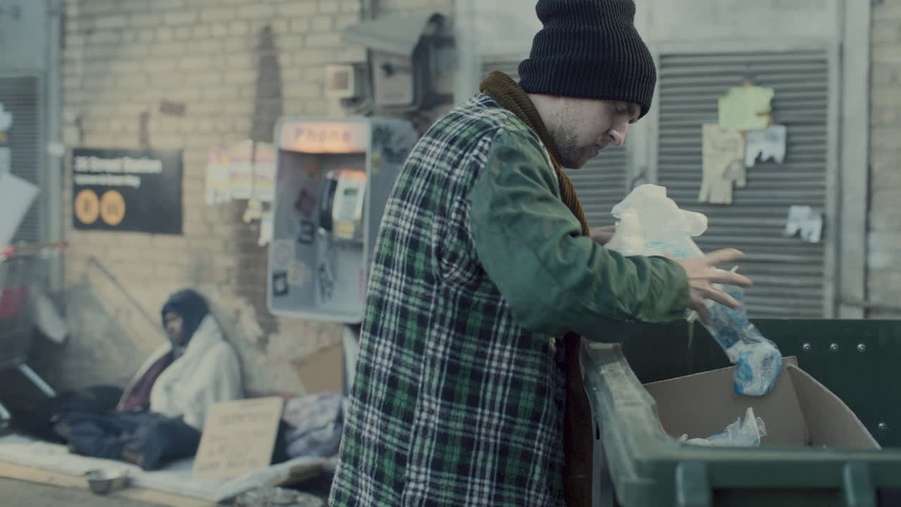 Homeless Man Digging through Trash Bin on Urban Street