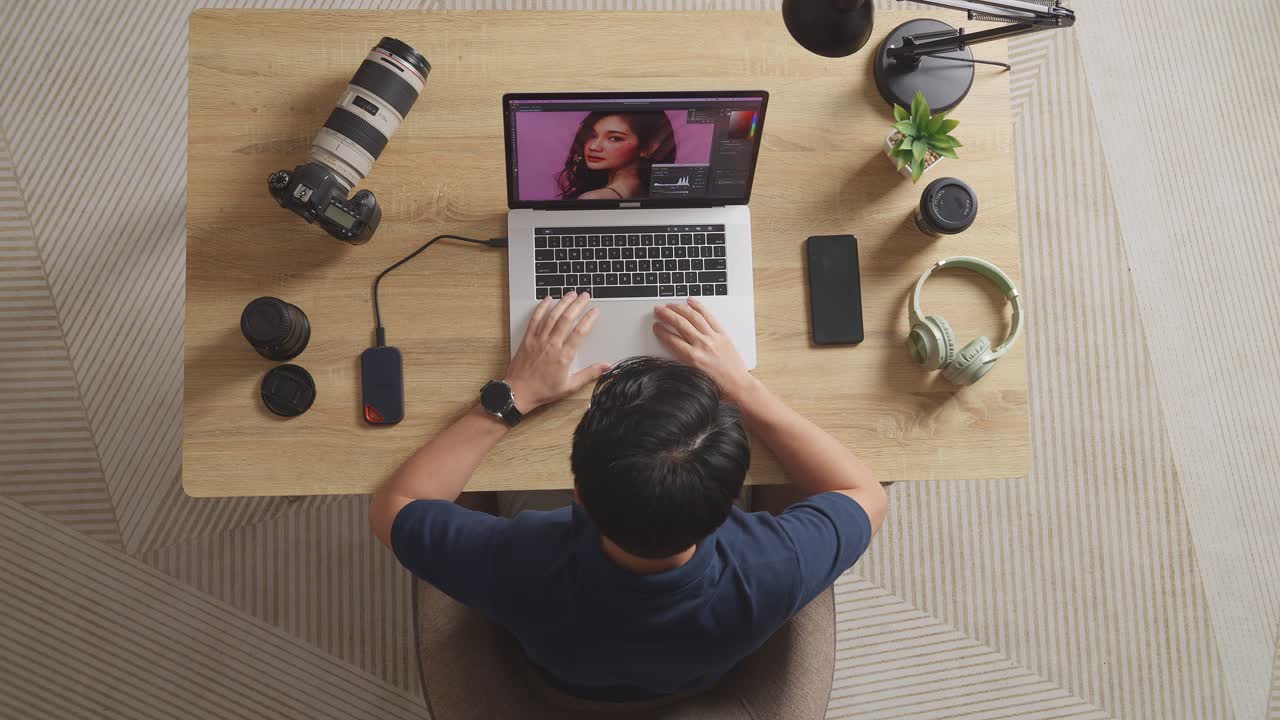 Top View Of A Male Editor Sitting In The Workspace Using A Laptop Next To The Camera Editing Photo Of A Female At Home