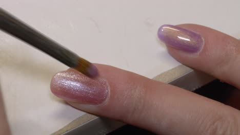 Close-up-shot-of-woman-apply-purple-pink-glitter-Nail-Polish-on-finger