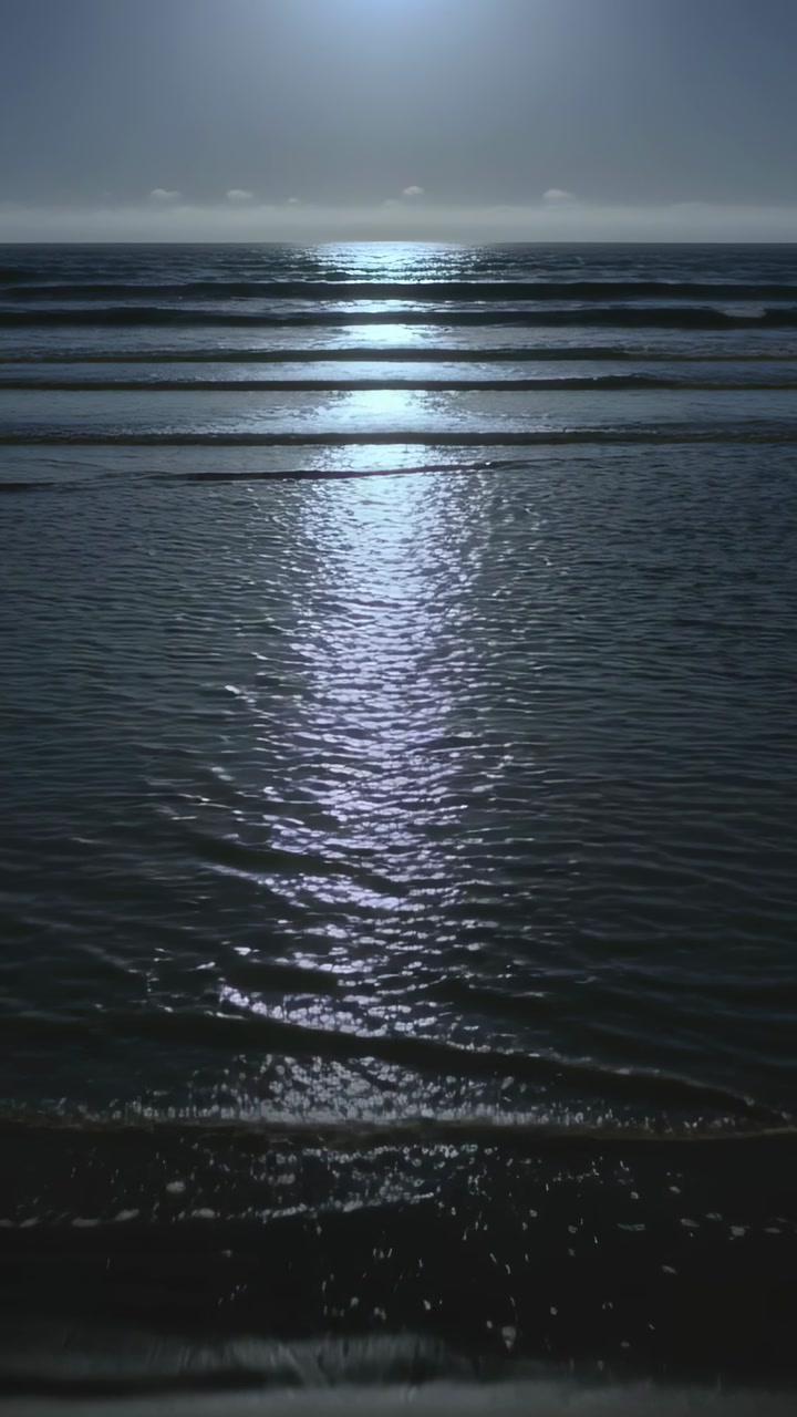 Vertical video: Casting bright horizon light, parallel wave bands rippling at shoreline with prints
