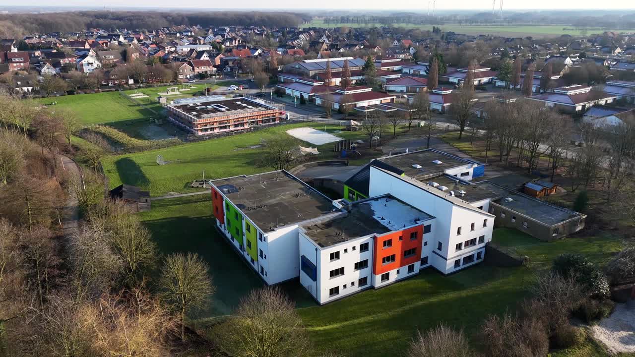High school building with colored facade of building during sunny day in winter season. Leafless trees in small american town. Aerial forward wide shot.