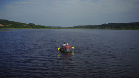 aerial view of grandfather and grandson floating on the boat on the picturesque river on a summer day