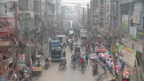 Numerous-cars,-motorcycles,-rickshaws,-and-pedestrians-driving-and-walking-through-a-busy-road-in-Dhaka,-Bangladesh