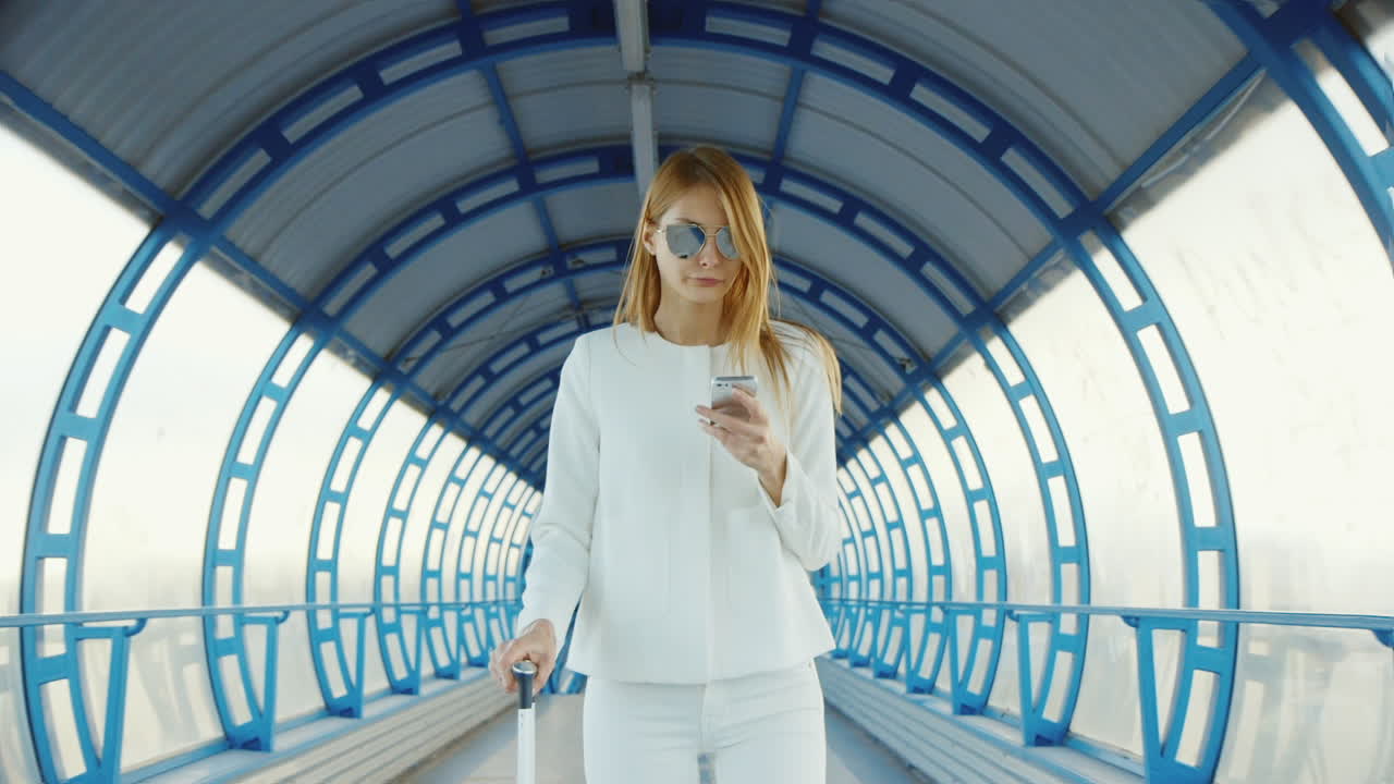 햇빛이 가득한 터널에서 이야기하는 비즈니스 여성은 여행 가방에 있는 전화기를 사용합니다.