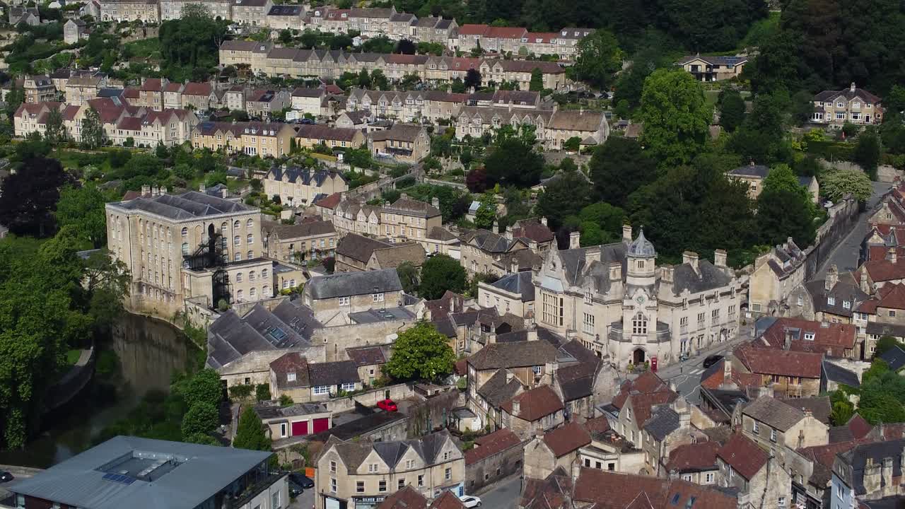 Drone moves forward above the historic town of Bradford-on-Avon, revealing stone buildings, narrow streets, and cars driving uphill through the city