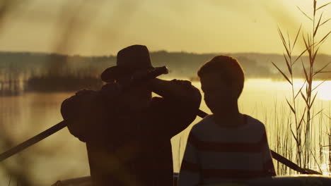 close view of senior man and his grandson sailing in a boat on the lake at sunset