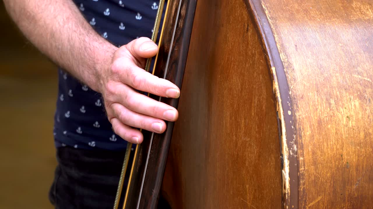 Street musican plays beautifully on double bass, contrabass on a summer day.