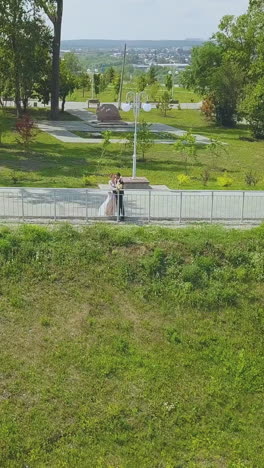 happy just married couple kisses near handrail in beautiful green park on sunny autumn day bird eye view