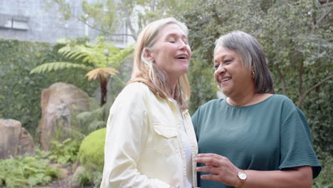 smiling multiracial senior female friends enjoying conversation and bonding in garden, copy space