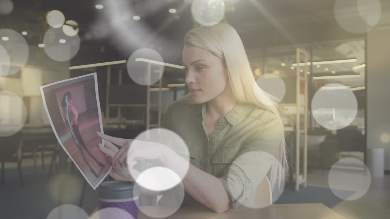 анимация светлых пятен над кавказской бизнесменкой, проводящей видеозвонок и показывающей фотографии