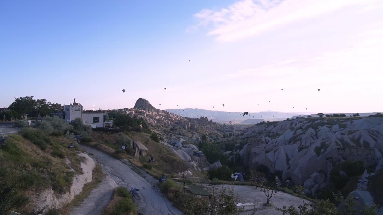 toma amplia en cámara lenta de bandada de pájaros volando a través del marco con montañas y globos de aire en segundo plano en uchisar, capadocia, turquía