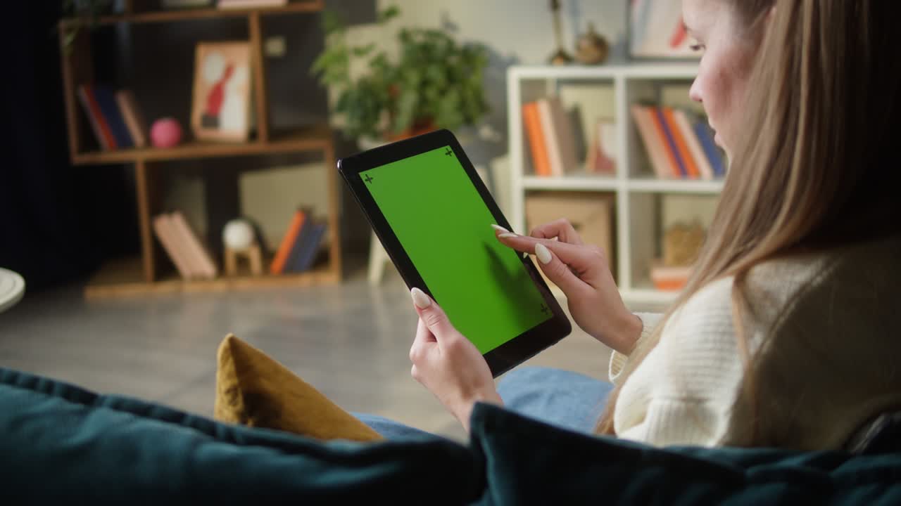 mujer usando una tableta de gadget con pantalla verde. persona femenina irreconocible deslizando la llave de croma, sentada en el sofá en la sala de estar. compras en línea, navegar por internet. tiempo libre en casa, ocio