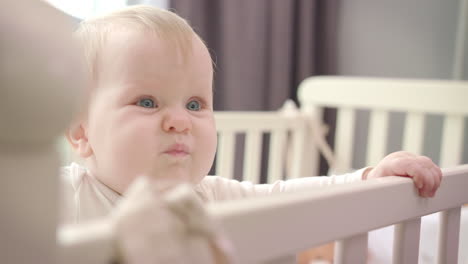 sad baby standing in bed. little baby emotion. toddler girl learn stand in bed