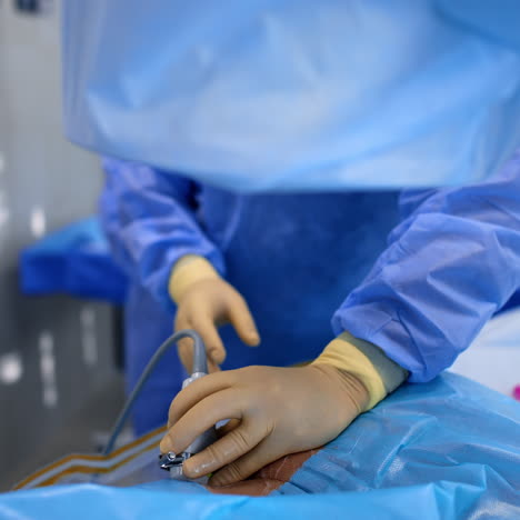 hands of doctor in latex gloves hold the ultrasound transducer attached to a patient. surgeon turns around to take a tool and input it into patient's body.