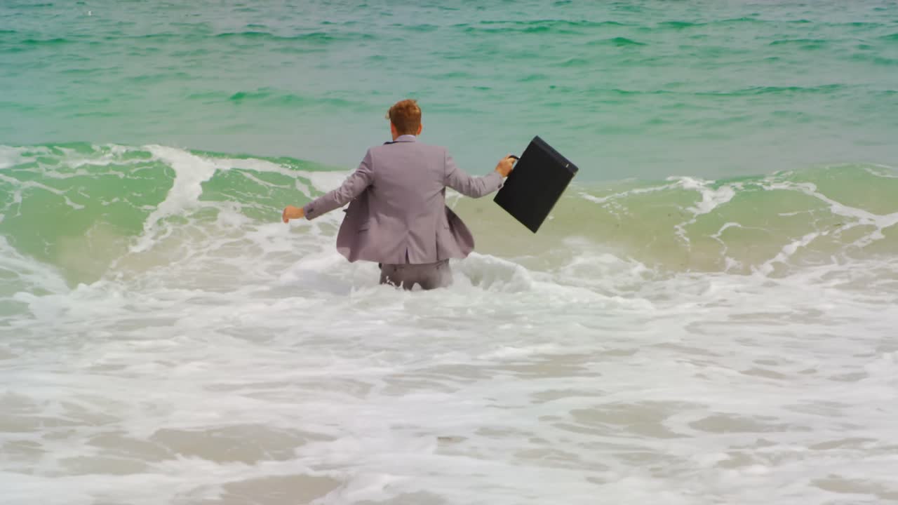 vista trasera de un hombre de negocios caucásico caminando con un maletín en el mar en la playa 4k