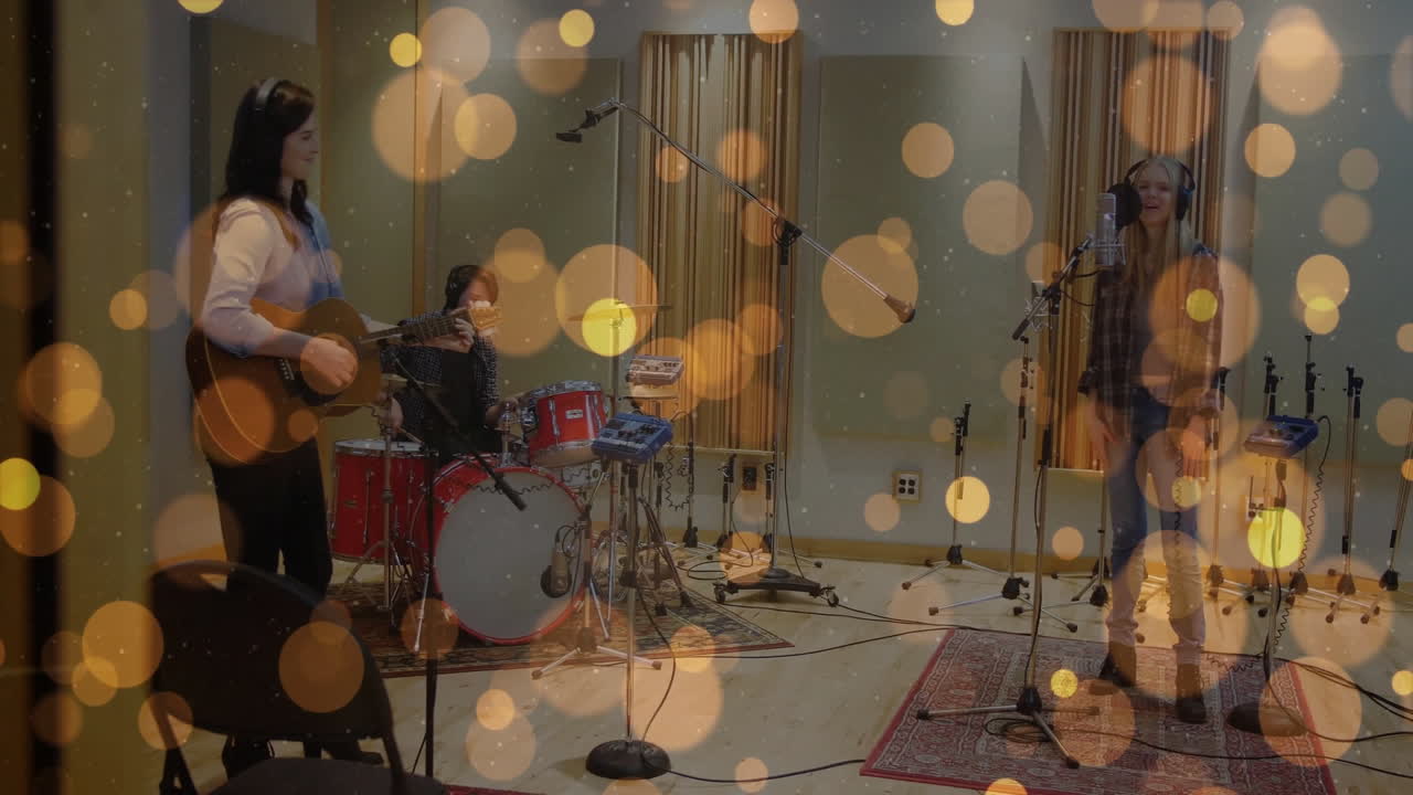 Bandmates playing guitar, drumming and singing into microphone in studio with golden bokeh floating
