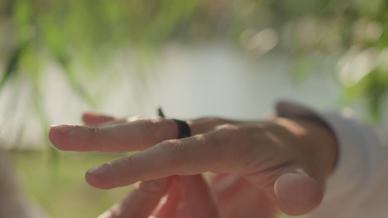 Closeup hand with wedding ring near leaf, lakeside sunlight and soft bokeh, gentle fingertip movement across green foliage, intimate promise gesture suggesting marital bond and family connection
