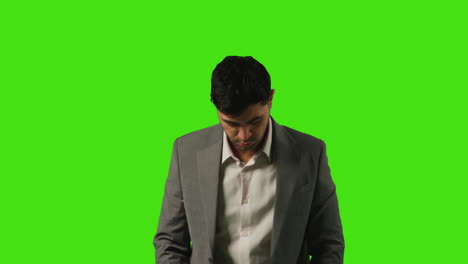 portrait of young businessman standing against green screen straightening and adjusting suit against green screen 2