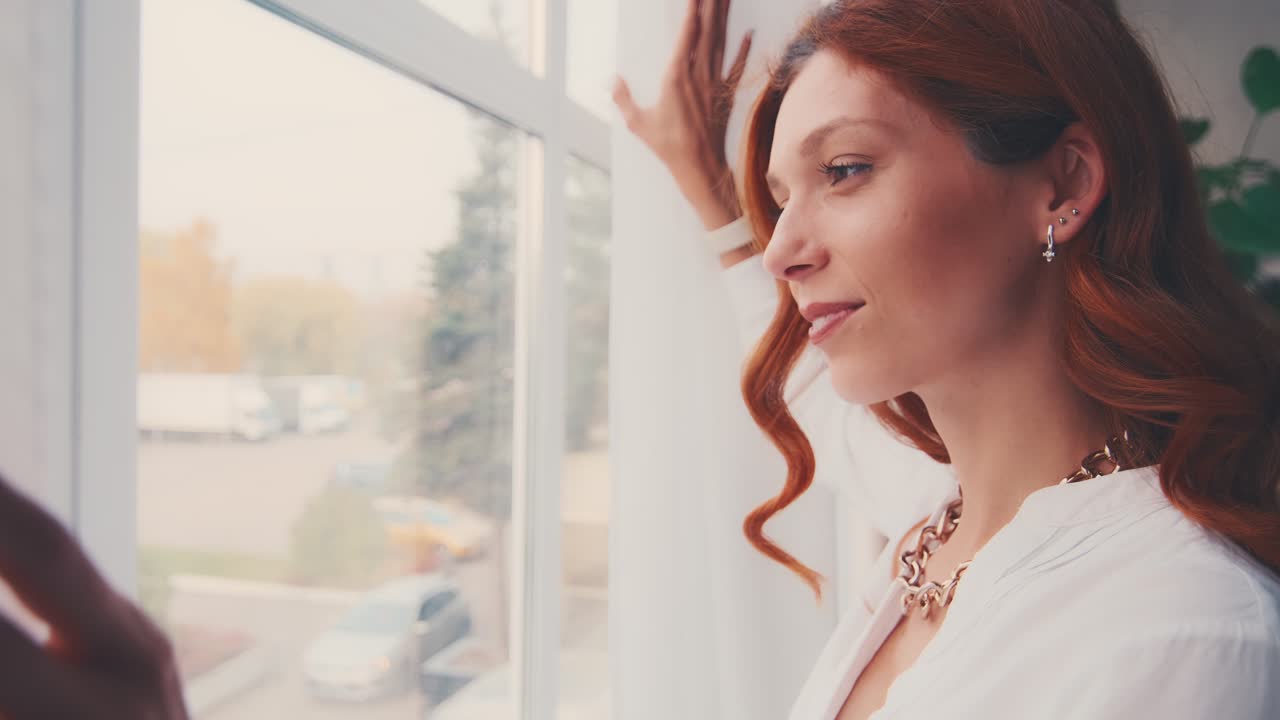 행복하고 낙관적인 젊은 여성이 창문을 통해 보는 커튼 렌즈를 열고