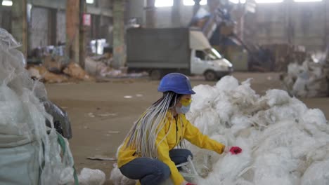 Waste-processing-plant.-Technological-process.-Recycling-and-storage-of-waste-for-further-disposal.-Woman-worker-in-hard-hat-gathering-from-the-floor,-pressing-used-plastic-tape-on-recycle-factory.-Slow-motion