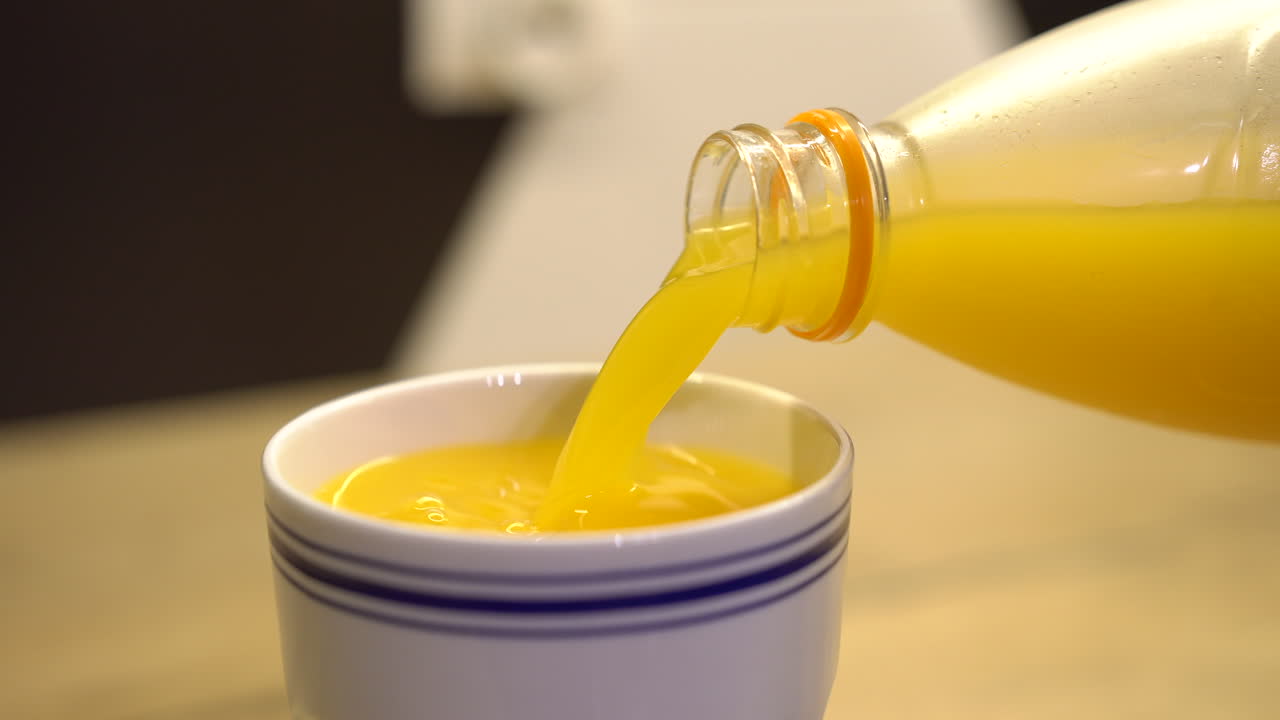 Versare succo d'arancia da una bottiglia di plastica in una tazza da caffè bianca con strisce blu