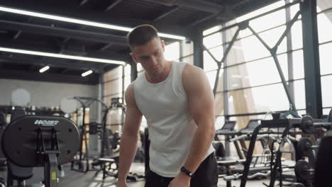 young man bends over to place towel on bench seat before adjusting gym machine controls highlighting routine equipment hygiene and prep steps in bright modern fitness center during workout session