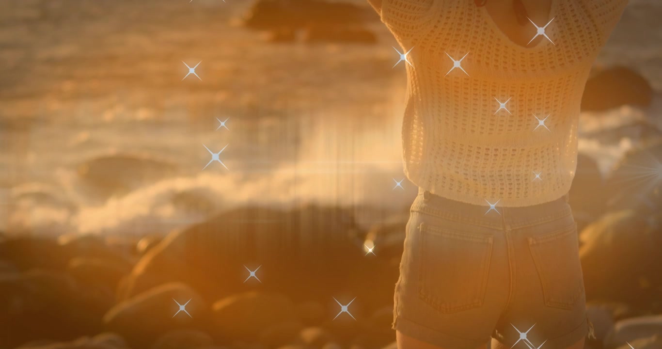 Animación de iconos de estrellas brillantes sobre la vista trasera de una mujer caucásica en las rocas cerca del mar.