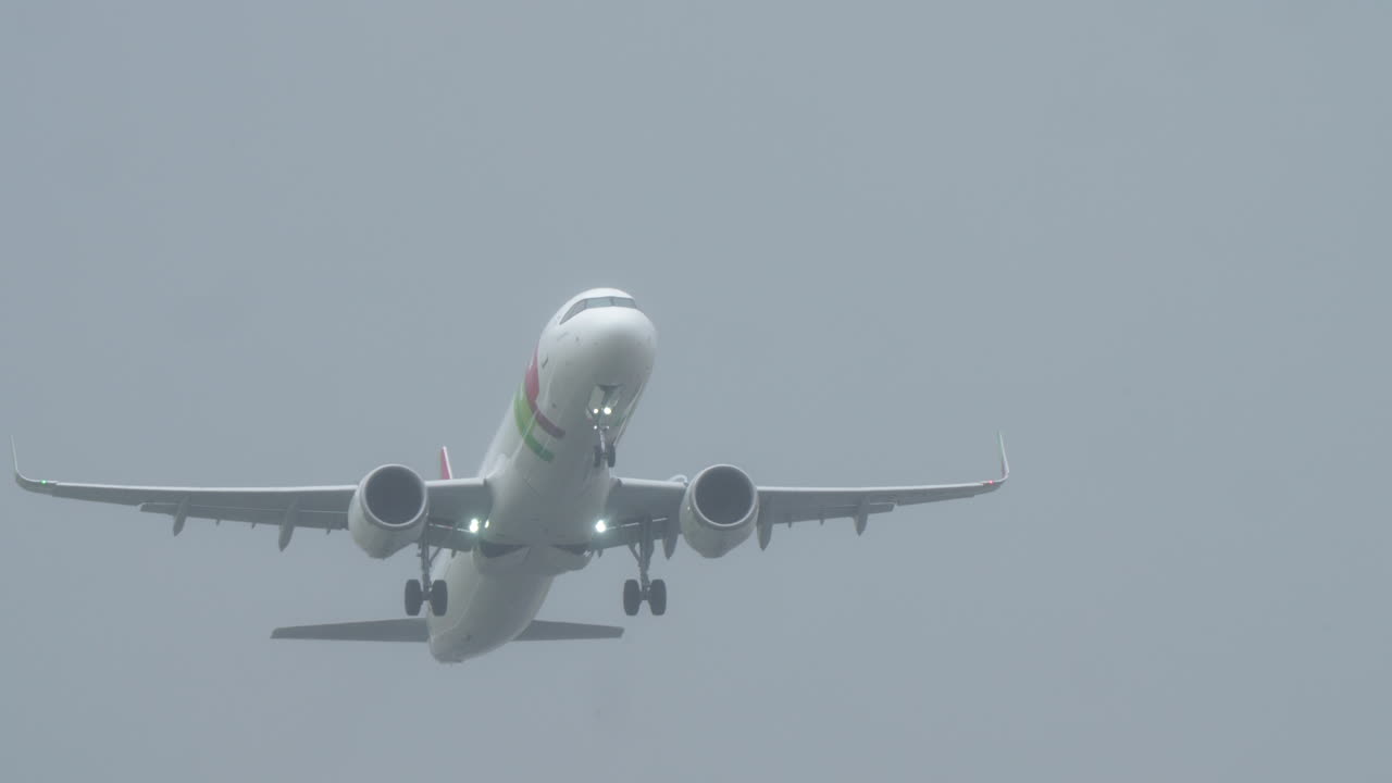 LISBON, PORTUGAL - APRIL 1, 2025: A TAP Portugal aircraft takes off at Humberto Delgado Airport in foggy weather conditions. The plane lights are on and a red-and-white windsock is visible on the right side of the runway