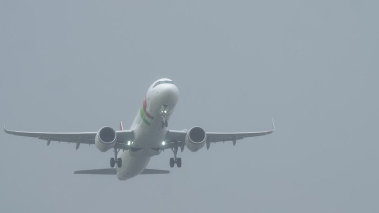 LISBON, PORTUGAL - APRIL 1, 2025: A TAP Portugal aircraft takes off at Humberto Delgado Airport in foggy weather conditions. The plane lights are on and a red-and-white windsock is visible on the right side of the runway