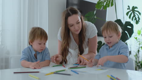 mom helps two sons of 2 and 4 years old to do preschool homework to draw a picture with pencils