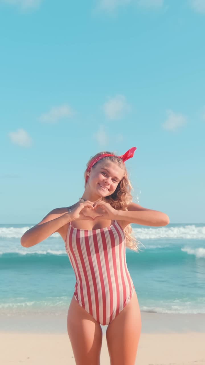Young attractive joyful caucasian woman teen shows hearts stands on sea beach