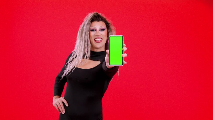 Drag queen che tiene in mano uno smartphone con schermo verde su sfondo rosso