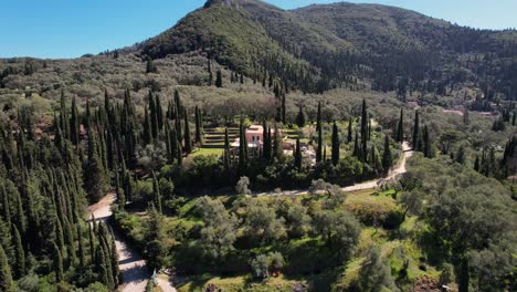 counter clockwise rotating shot of small, colorful house in between cypresses of the forest covered mountains of corfu