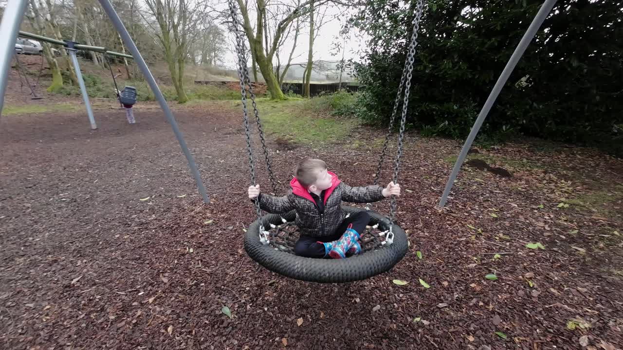 niño divirtiéndose en un patio de recreo balanceándose y riéndose rodeado de hojas de otoño