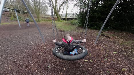 young boy having fun in a playground swinging and laughing surrounded by autumn leaves