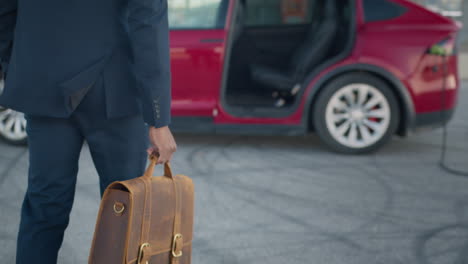 businessman with briefcase in front of electric car