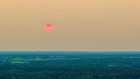 drone hyperlapse of bright pink sun setting behind forest horizon under warm hazy sky