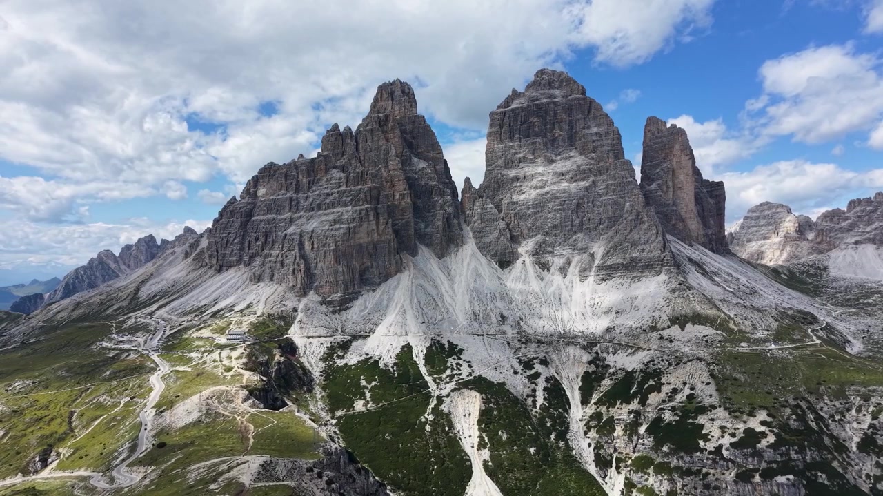 Vista cinematografica da drone che mostra le iconiche Tre Cime di Lavaredo che si ergono sopra il paesaggio alpino aspro nelle Dolomiti, Italia.