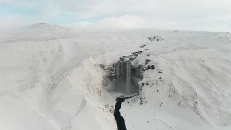 A-beautiful-large-waterfall-in-Iceland-in-mid-winter-covered-by-the-snow-around-it-and-the-clouds-makes-it-even-better