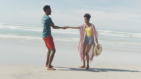 happy african american couple walking and holding hands on sunny beach