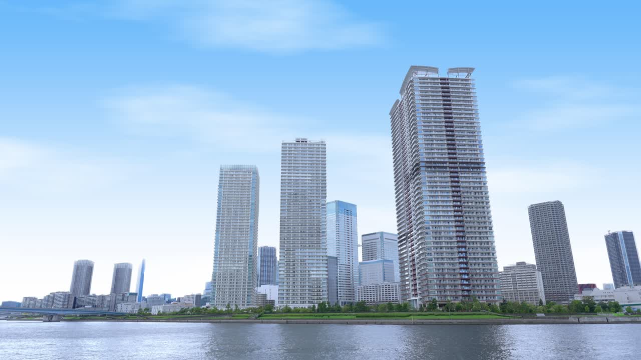 A peaceful wide shot of the Tokyo skyline from a waterfront promenade with modern high-rise buildings and a clear sky