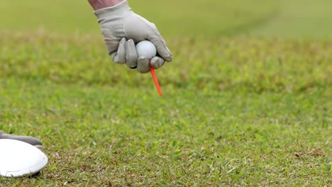 a golfer's gloved hand carefully places a golf ball on a tee on the grass.