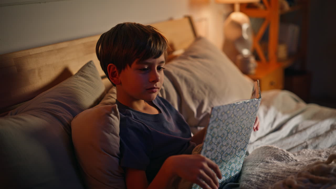 Relaxed boy reading bedtime lying evening bedroom closeup. Little child relaxing