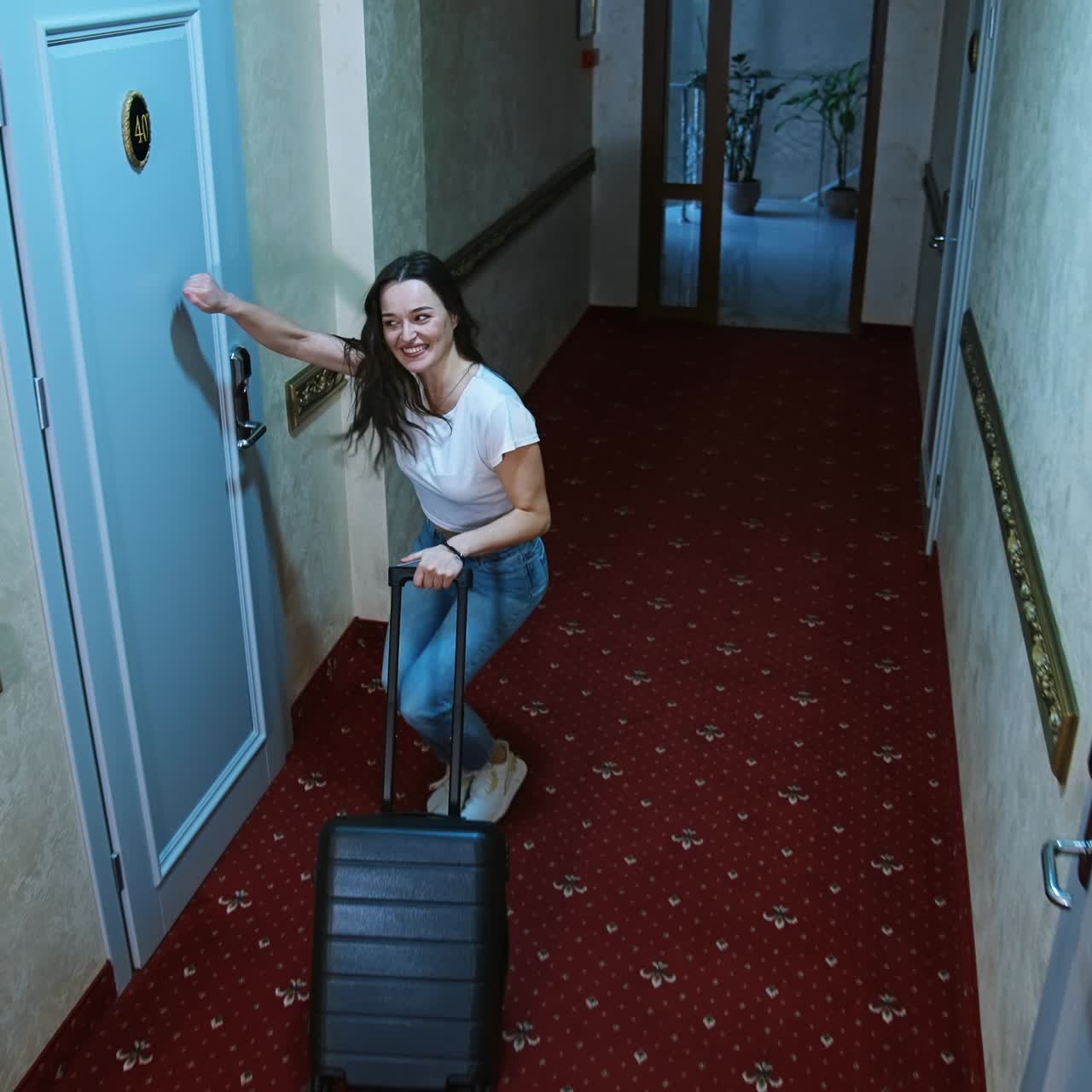 Woman holding a suitcase in hotel corridor. Cute happy girl moved in a hotel and is looking for her room