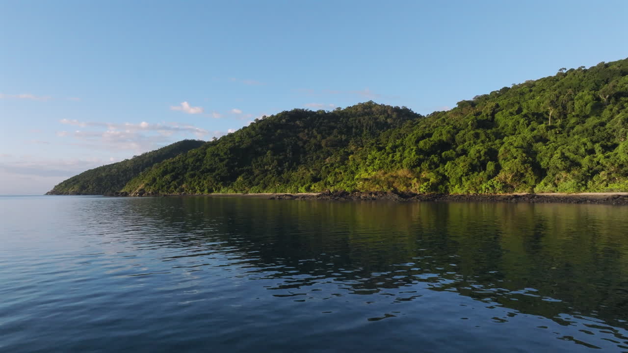 Drone flying towards a tropical island and then down the rocky coastline in the Whitsunday Islands, QLD, Australia