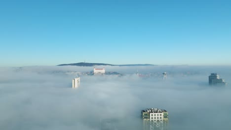 드론이 뒤로 미끄러지면서 빛으로 빛나는 공중 여행, 브라티슬라바 성과 밀집된 역전 구름을 통해 나타나는 건물을 포착합니다.