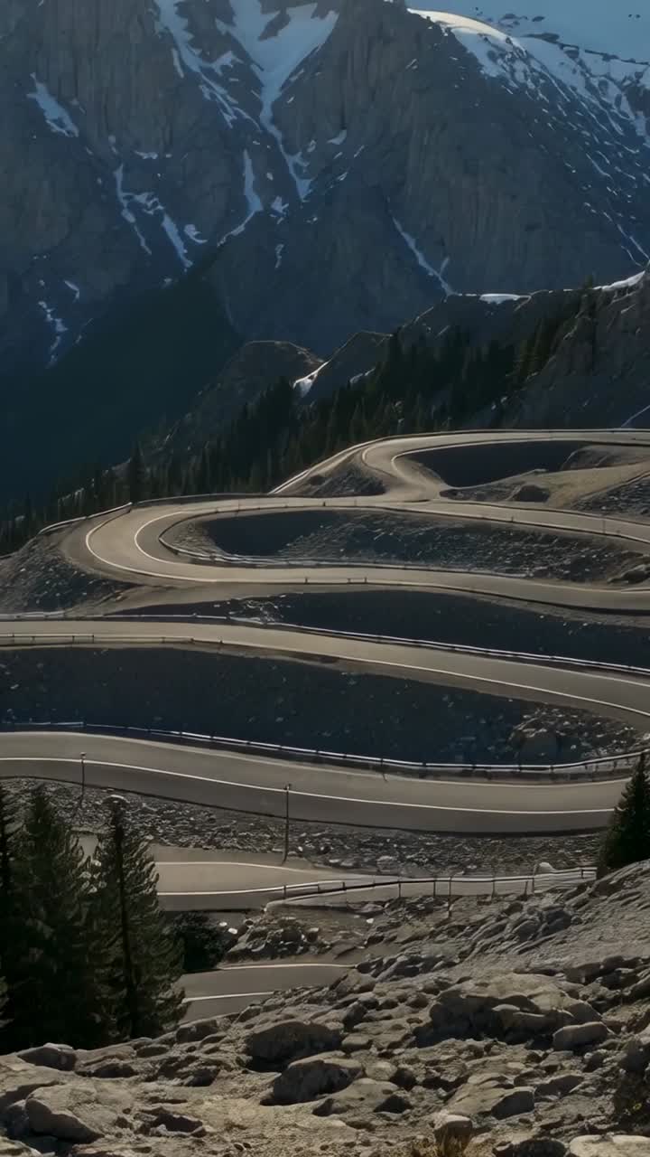 Vertical video: Camera panning revealing hairpin road climbing alpine pass, showing guardrail, snow