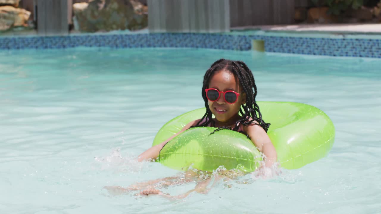 feliz chica afroamericana con gafas de sol nadando con anillo inflable en la piscina